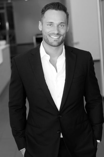 Confident man in a black suit smiling in an office setting.