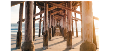 View under a wooden pier with sunlight and ocean waves.